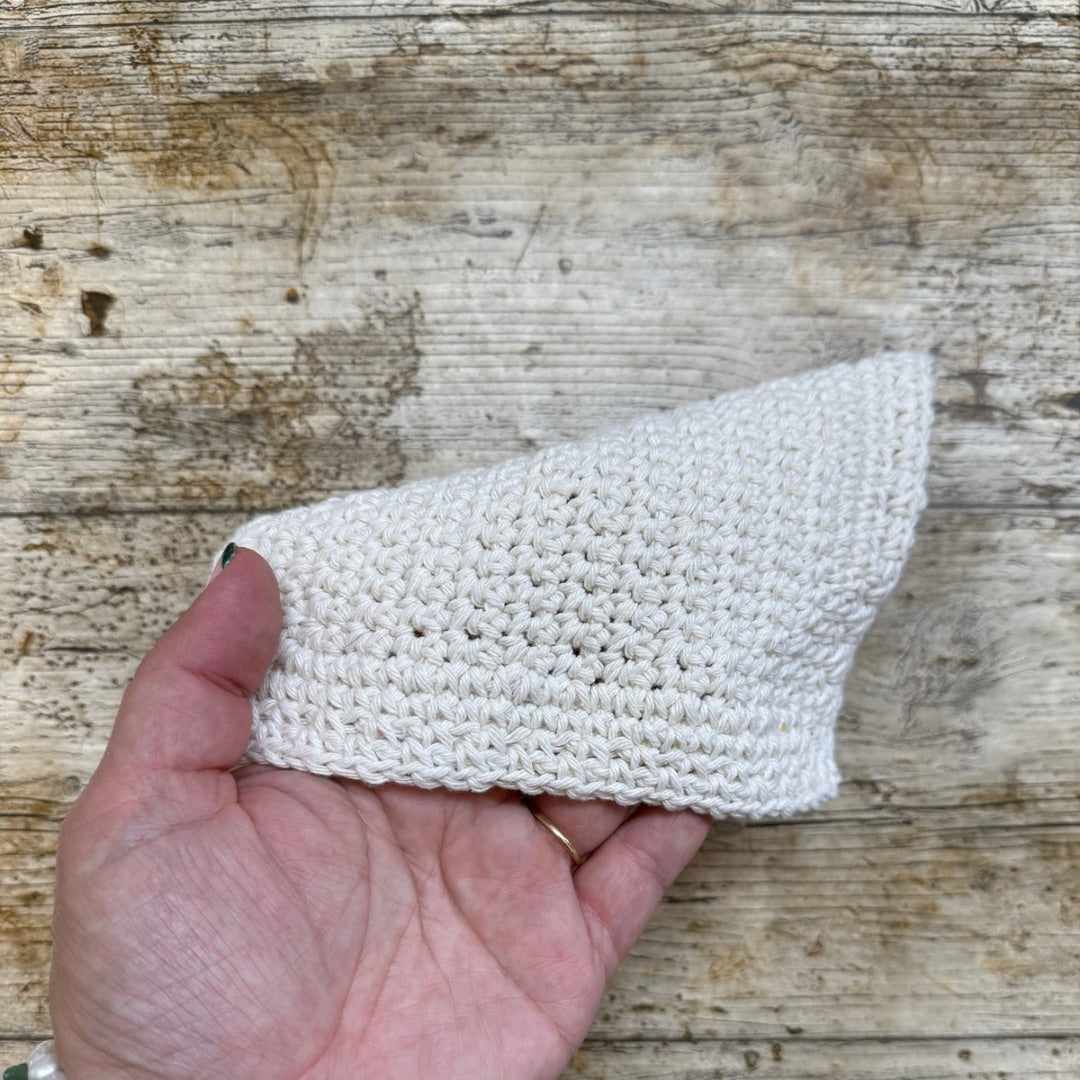 Hand holding a white crocheted dishcloth against a wooden background