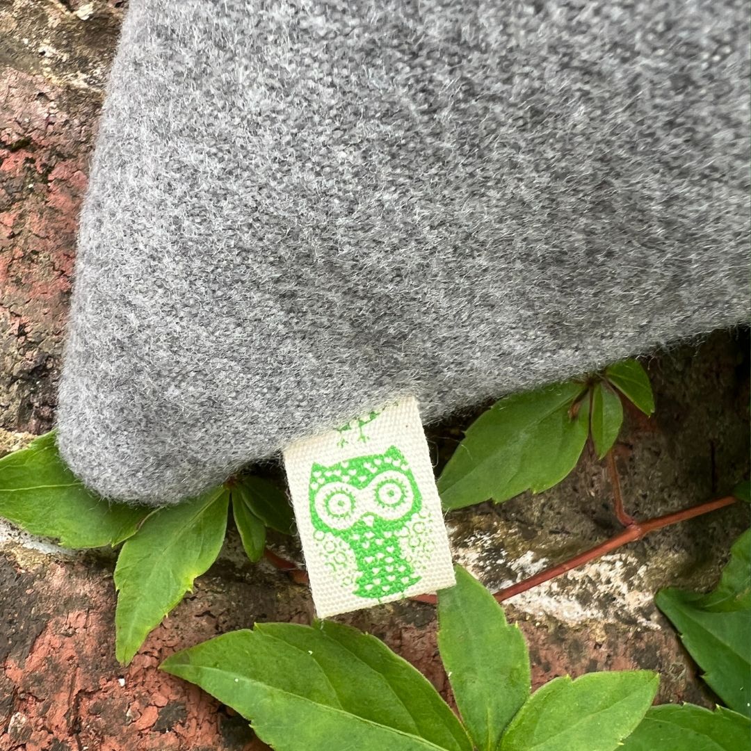 Gray fabric with a green tag featuring an owl design, surrounded by green leaves on a textured surface.
