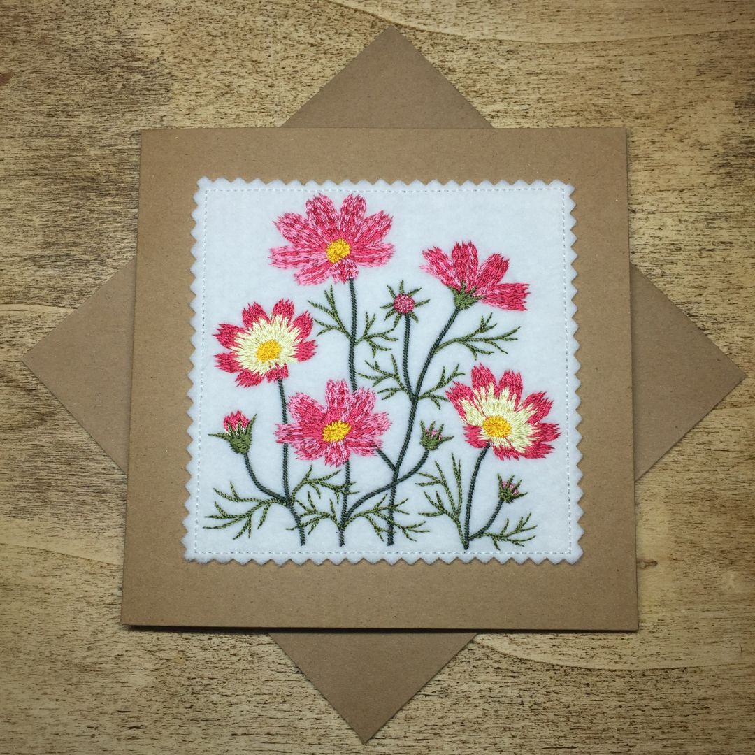 Embroidered card with pink flowers on a wooden surface