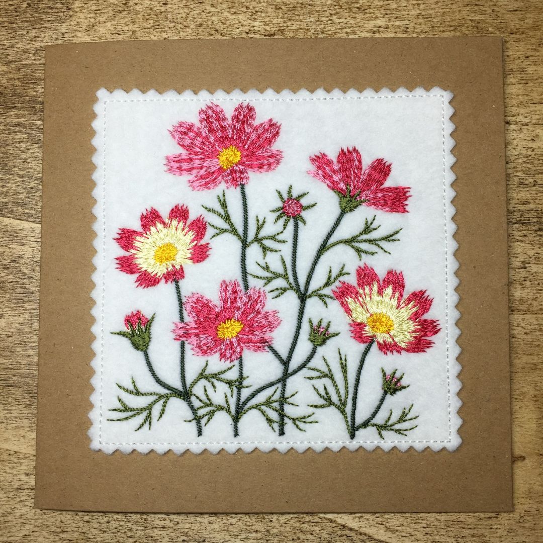 Embroidered floral design on a brown card with a wooden surface background