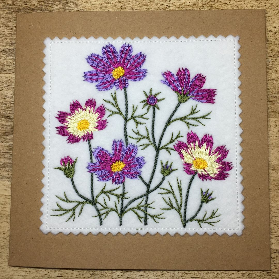 Embroidered floral design on a white fabric square with a brown border.