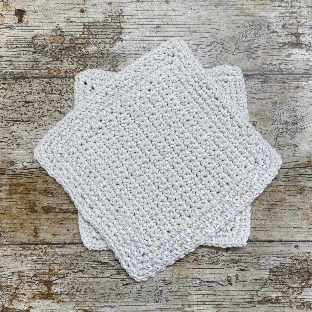 Two crocheted white hexagonal dishcloths on a wooden surface