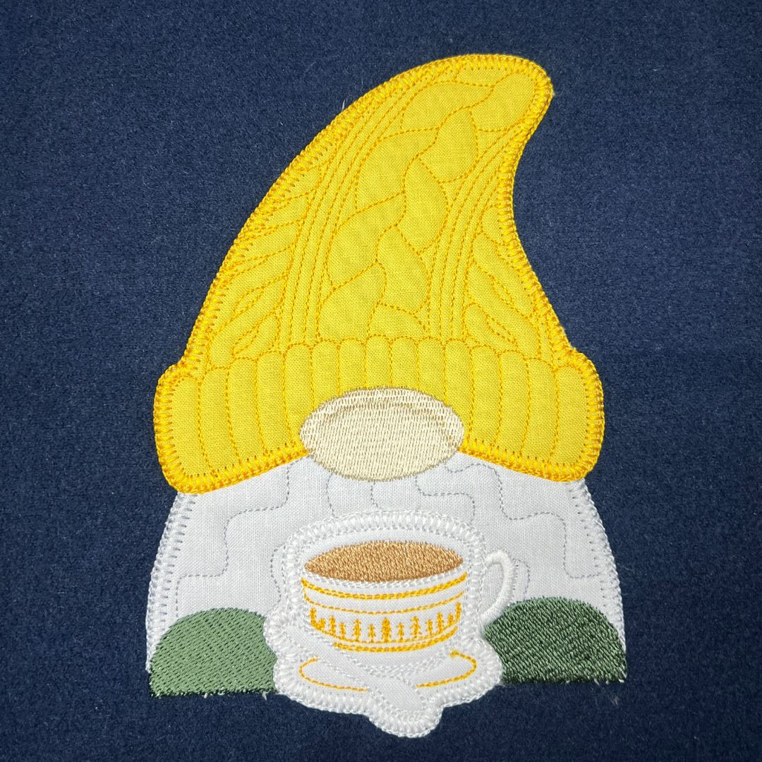 Embroidered patch of a gnome with a yellow hat and cup on a dark blue fabric background