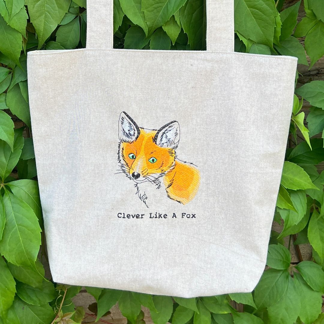 Tote bag with a fox illustration and 'Clever Like A Fox' text on a green leaf background