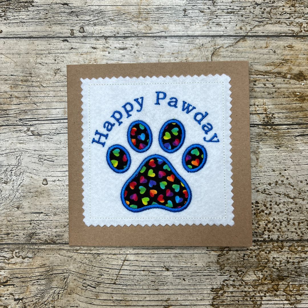 Card with 'Happy Pawday' text and paw print design on a wooden surface