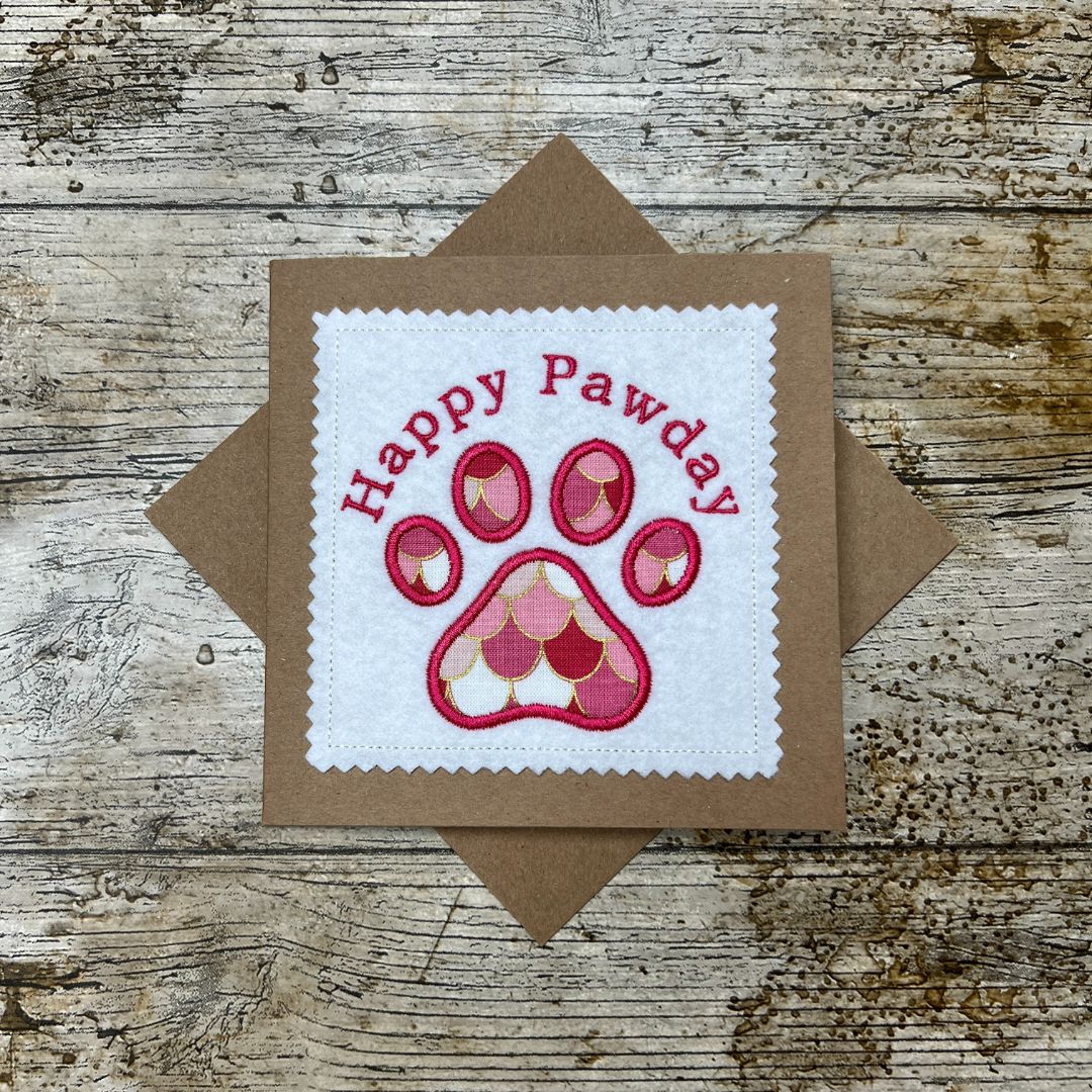 Card with 'Happy Pawday' text and paw design on a wooden surface