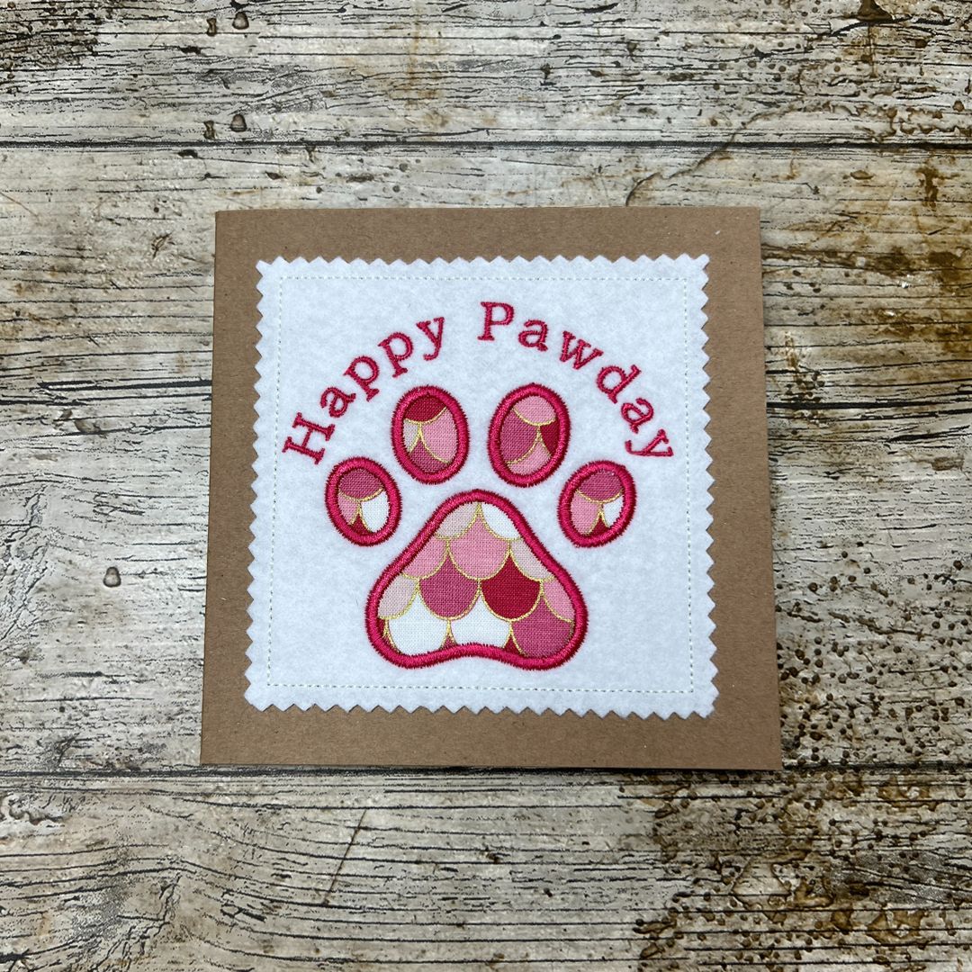 Card with 'Happy Pawday' text and paw print design on a wooden surface