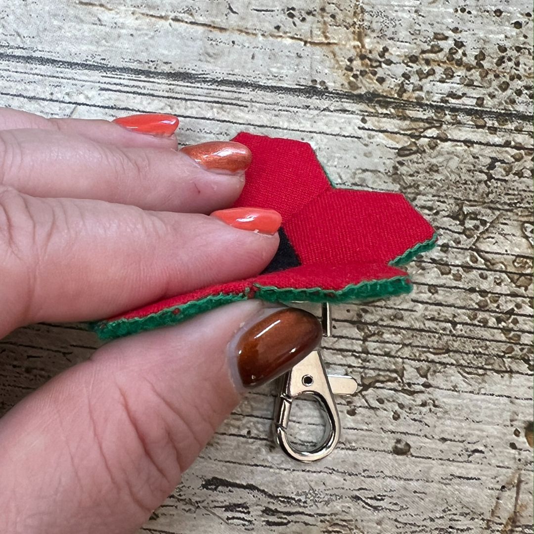Red fabric bow with a gold clasp held by a hand on a textured surface