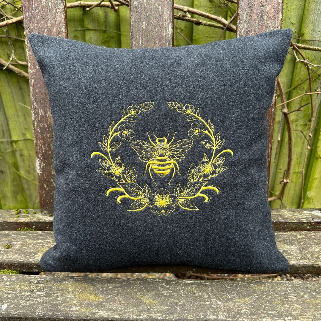 Black pillow with yellow bee design on a wooden bench
