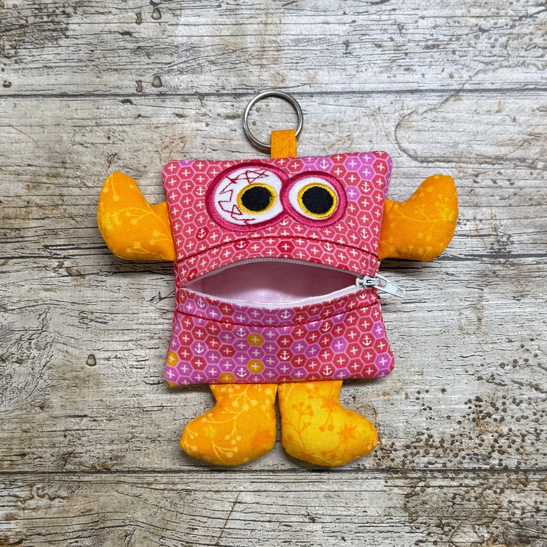 Pink and yellow money monster purse pouch with a zipper on a wooden surface