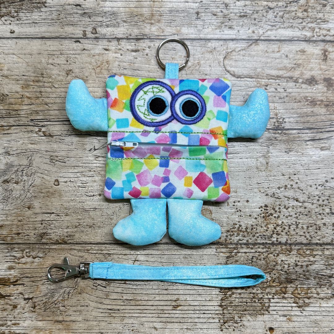 Colourful monster-shaped children's purse with blue arms and legs with a zipper on a wooden surface, with a wrist strap