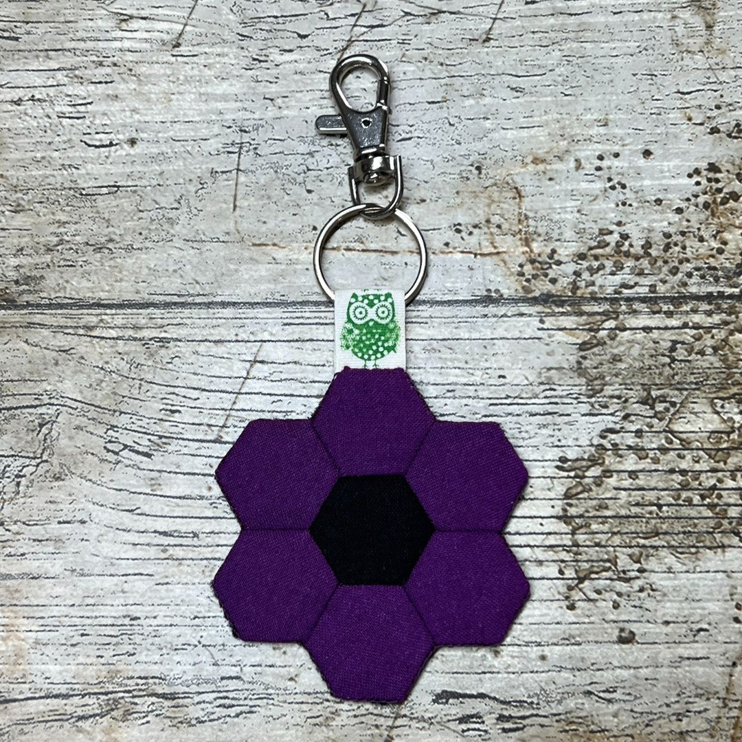 Purple flower-shaped keychain with a green owl design on a textured surface