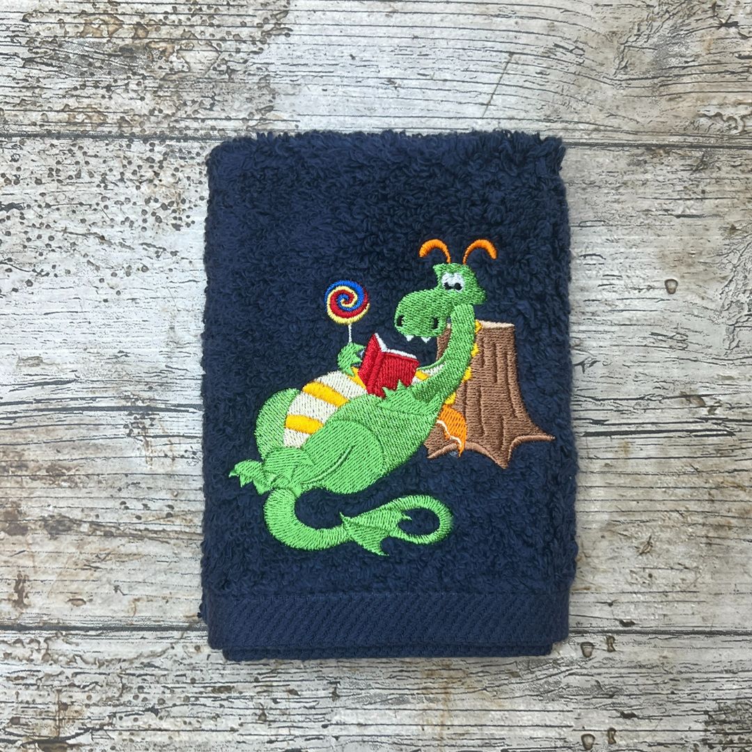Navy blue towel with a green dragon reading a book design on a wooden surface