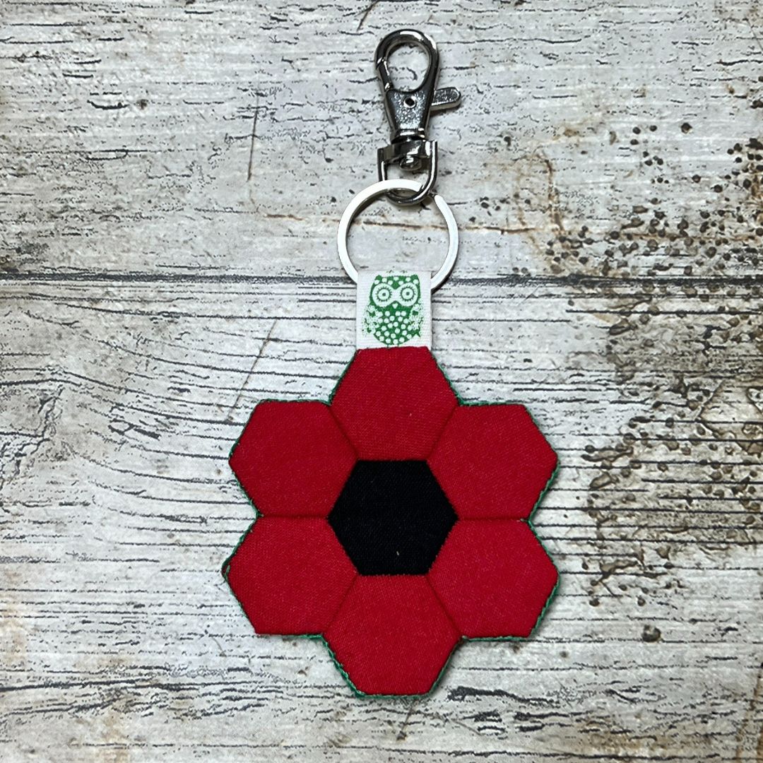 Red hexagonal flower-shaped keychain with a black center on a textured surface
