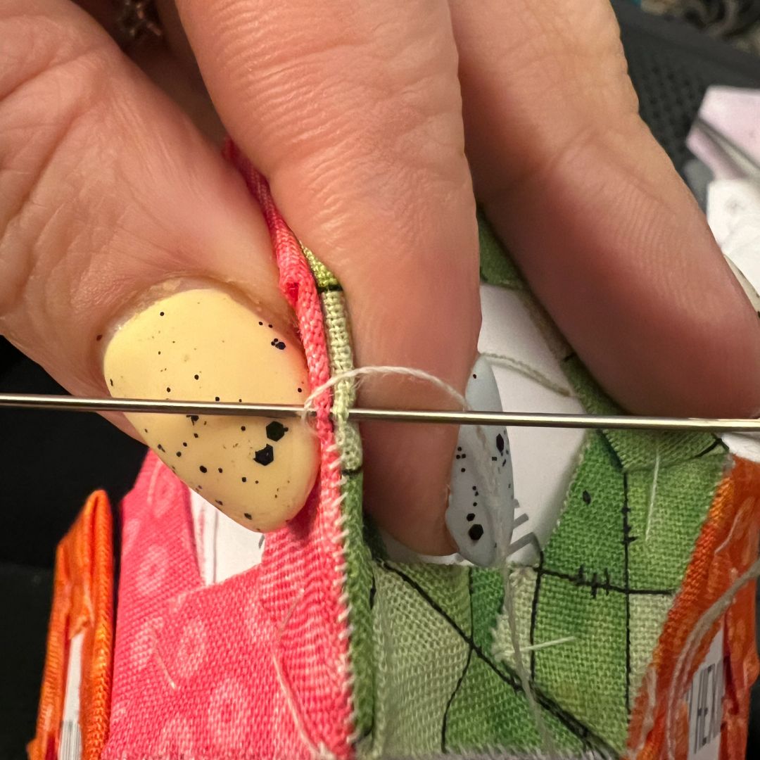 Close-up of hands threading a needle with colorful fabric in the background