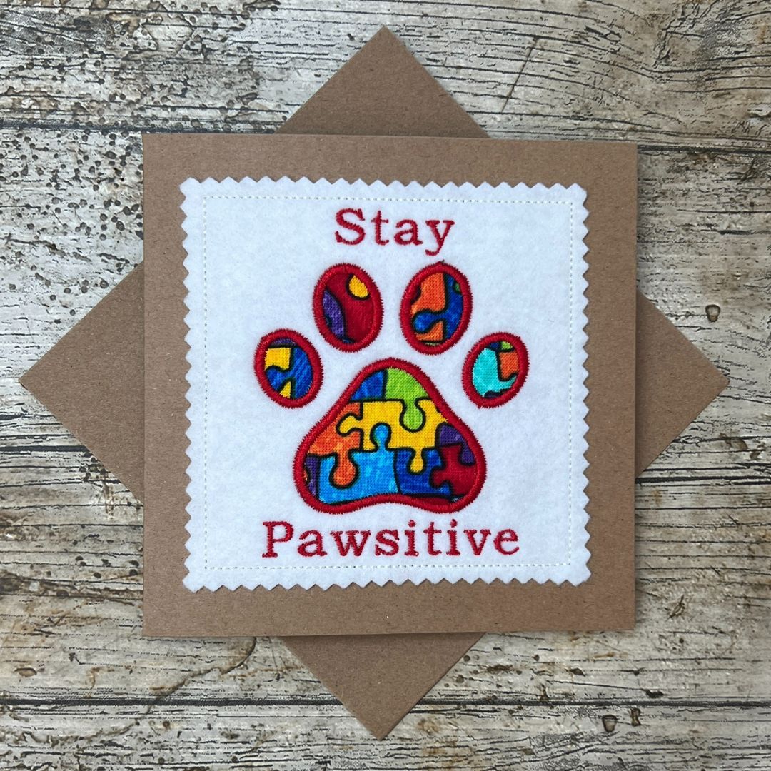 Card with colorful paw print and text 'Stay Pawsitive' on a wooden surface
