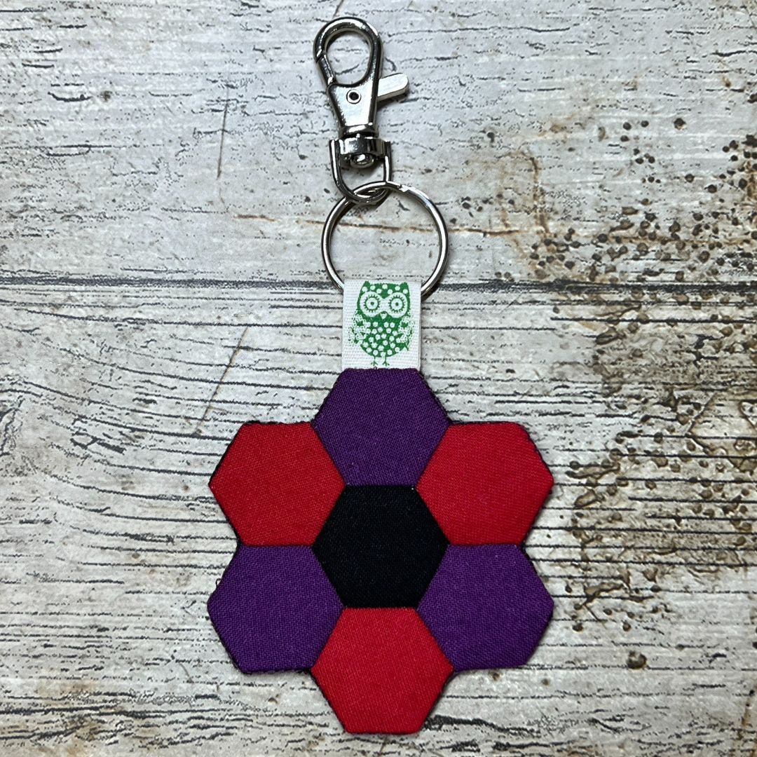 Hexagonal keychain with purple and red colors on a textured surface