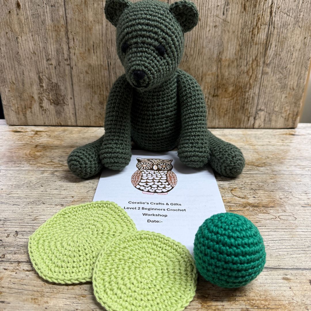 Crocheted bear and coasters & Ball on a wooden surface with a workshop flyer.