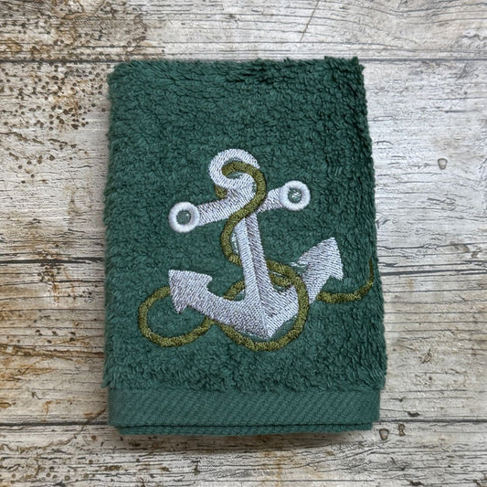Green towel with an embroidered anchor design on a wooden surface