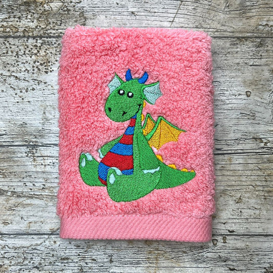 Pink towel with a green baby dragon design on a wooden surface