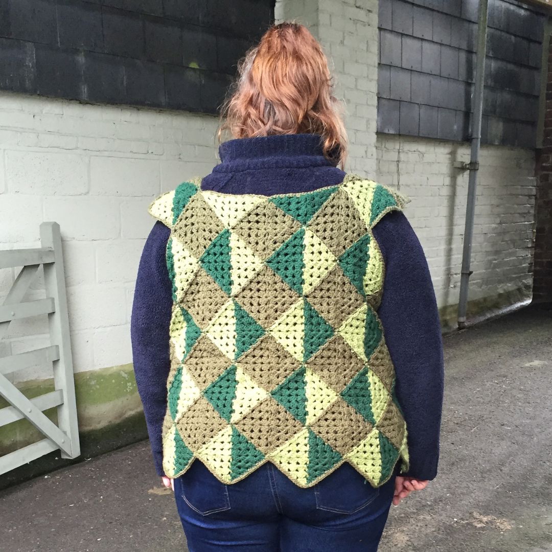Person wearing a green crocheted vest against a brick wall.