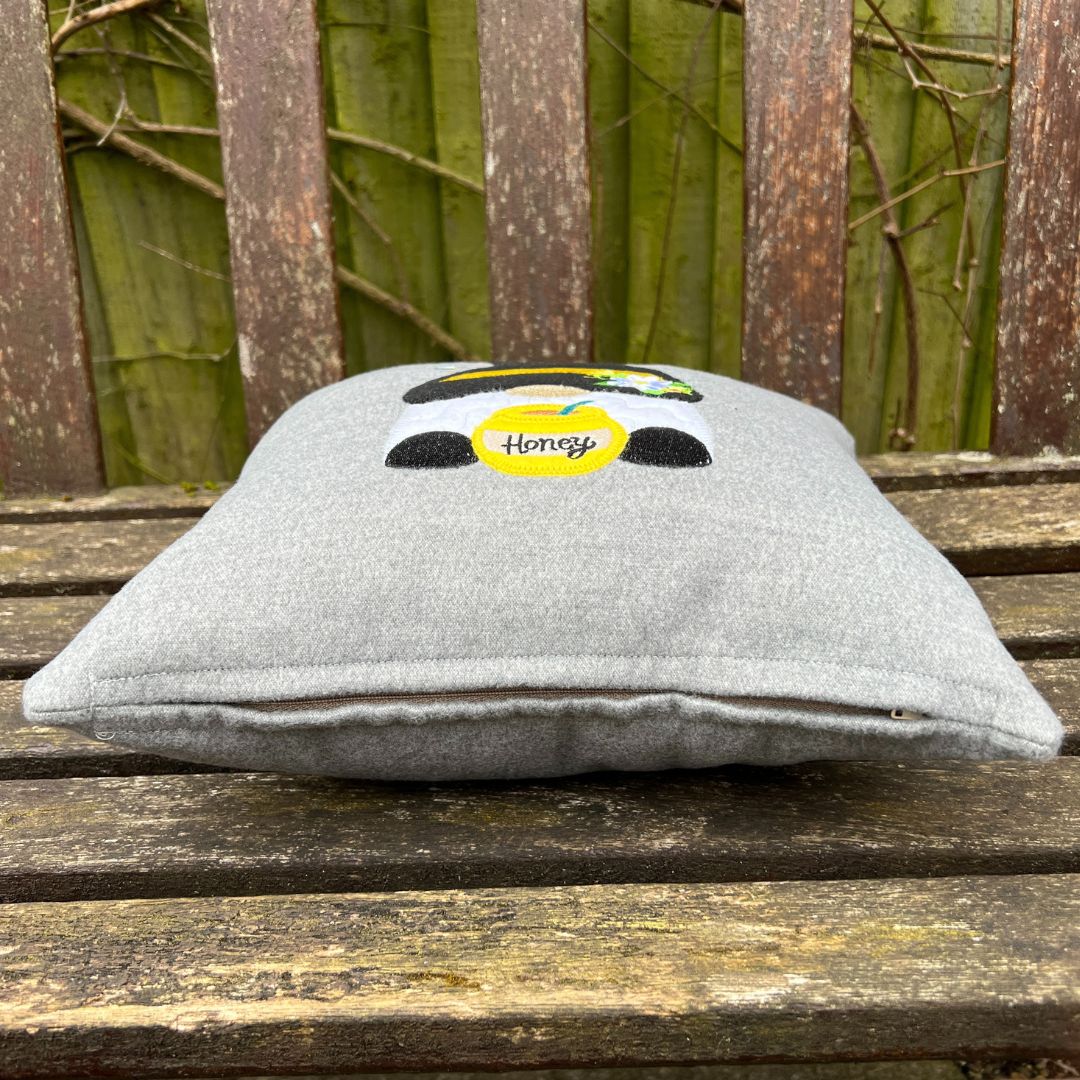 Gray pillow with a cartoon bee design on a wooden surface