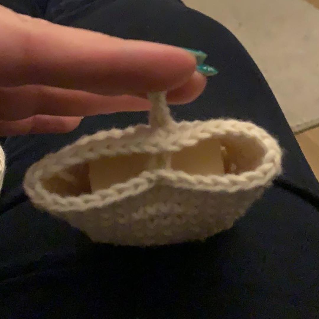 A close-up of a hand holding a small cream crocheted soap cozy with a handle, resting on dark clothing.