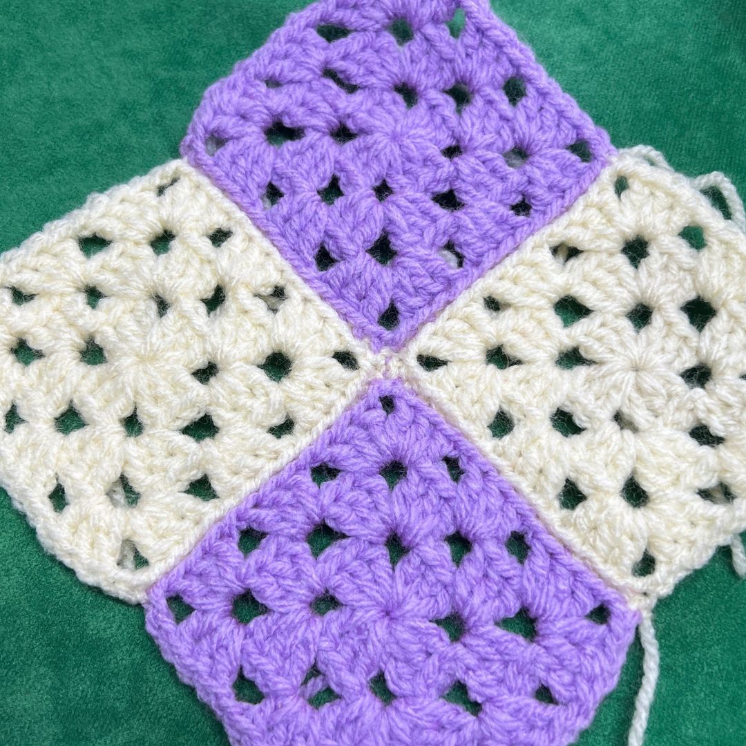 Four crocheted squares in purple and white on a green background