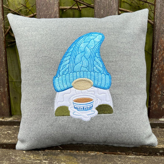 Gray pillow with a gnome holding a coffee cup design on a wooden surface.
