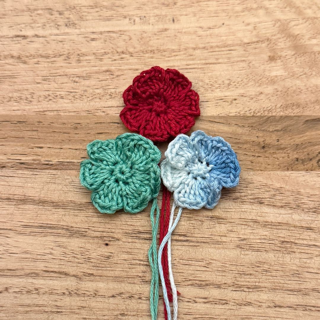 Three crocheted flowers in red, green, and blue on a wooden surface