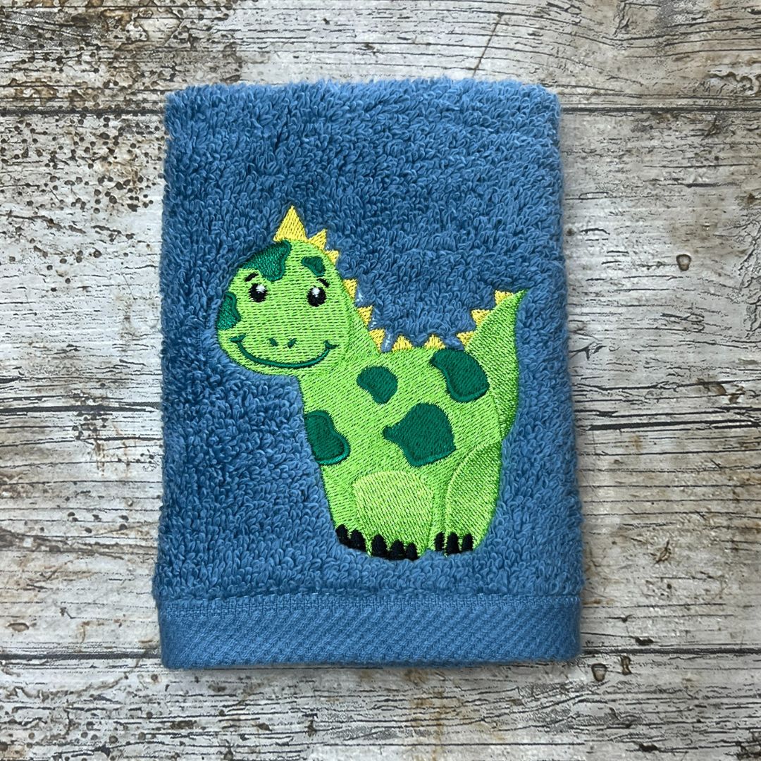 Blue towel with a green dinosaur design on a wooden surface