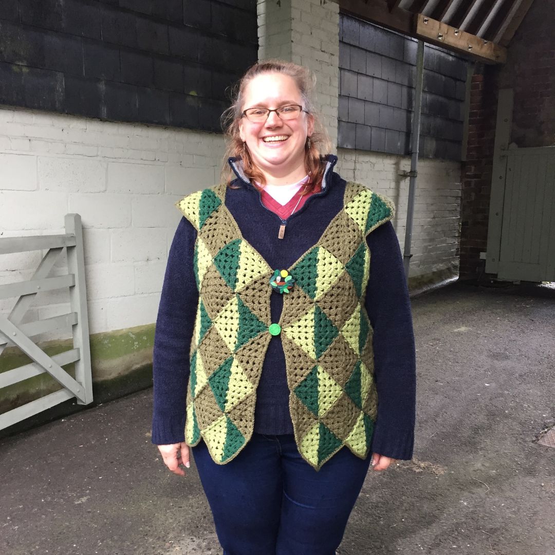 Person wearing a green crocheted waistcoat outdoors.