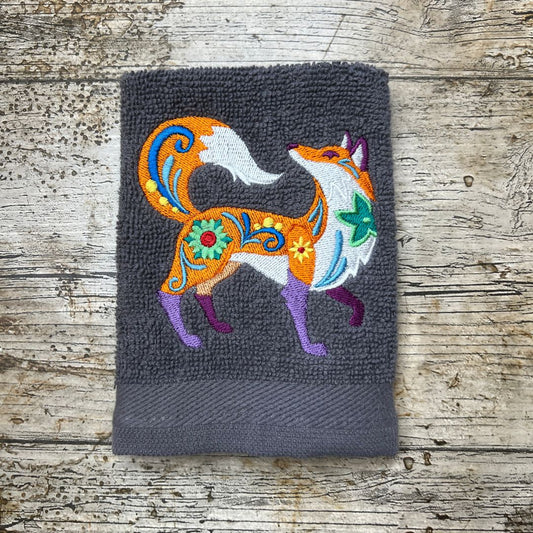 a Funky fox embroidered onto a  face cloth and place on a wooden background, made by Coralie's crafts & Gifts in Dorset.