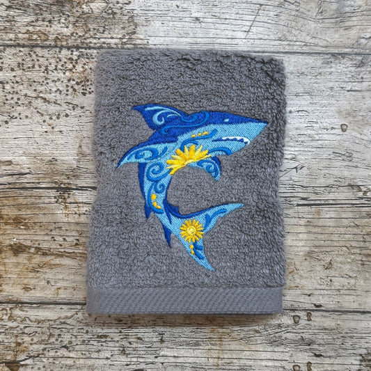 Beautiful bright funky shark design embroidered onto a steel face cloth sat on top of a wooden background. This is made at by Coralie at Coralie's Crafts & Gifts in Dorset