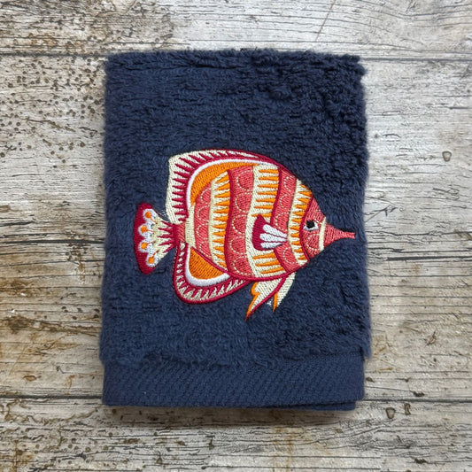 Beautiful funky fish design embroidered onto a face cloth and placed on a wooden background