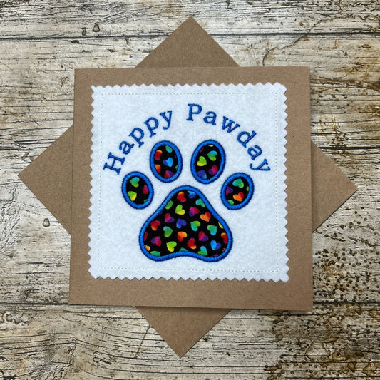 Card with 'Happy Pawday' text and paw print design on a wooden surface