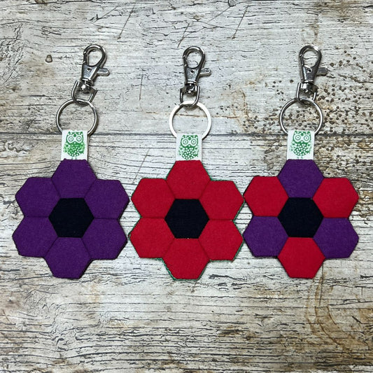 Three hexagonal keychains with purple, red, and a mix of both colors on a wooden surface.