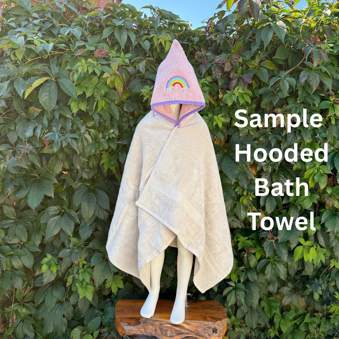 Hooded bath towel with a pink hood featuring a rainbow design, displayed against a green leafy background.