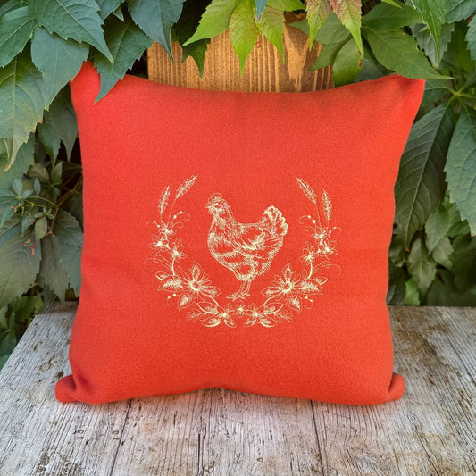 Beautiful embroidered chicken on a rusty orange cushion displayed on a wooden board with ivy hanging down behind it