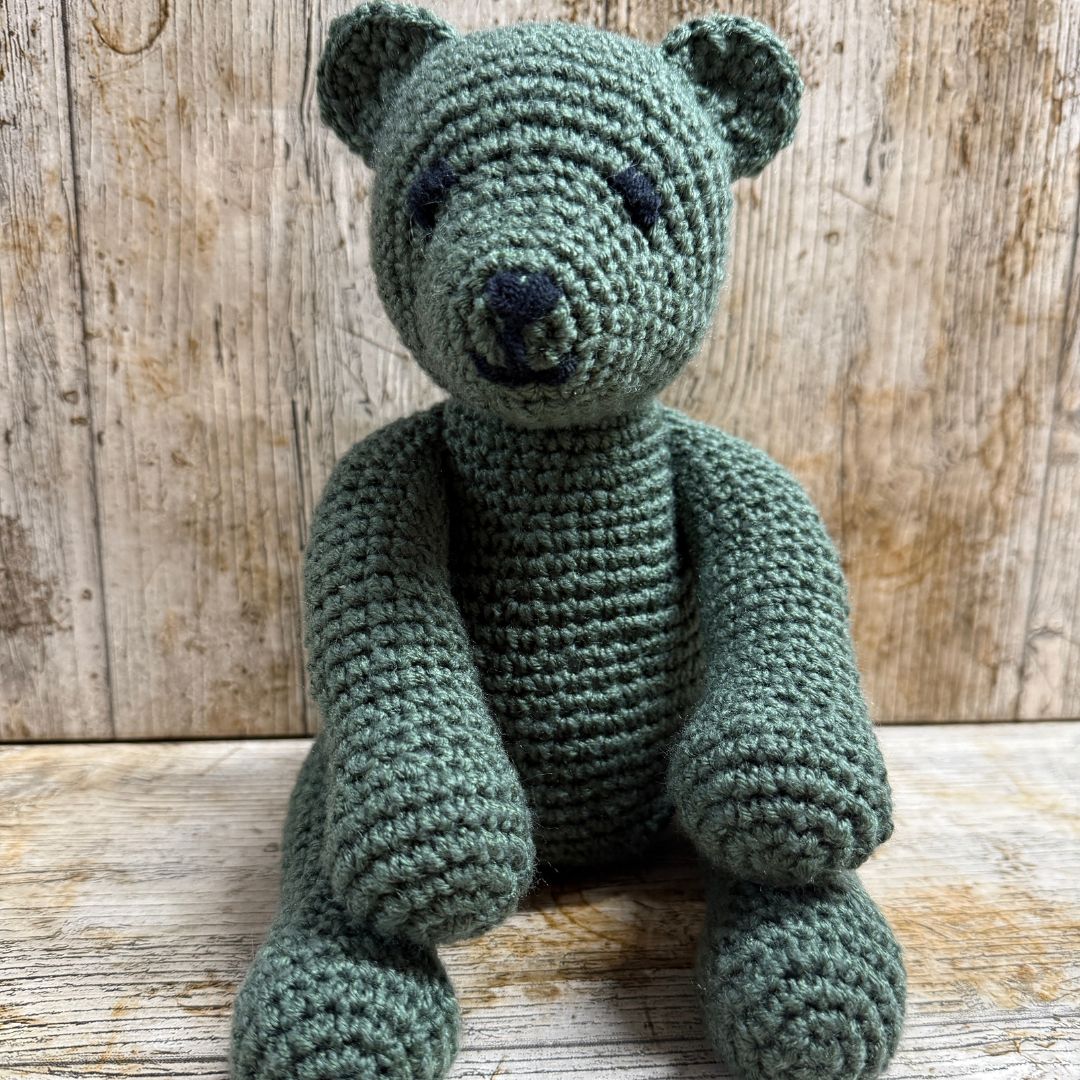 Crocheted bear toy on a wooden surface with a wooden background