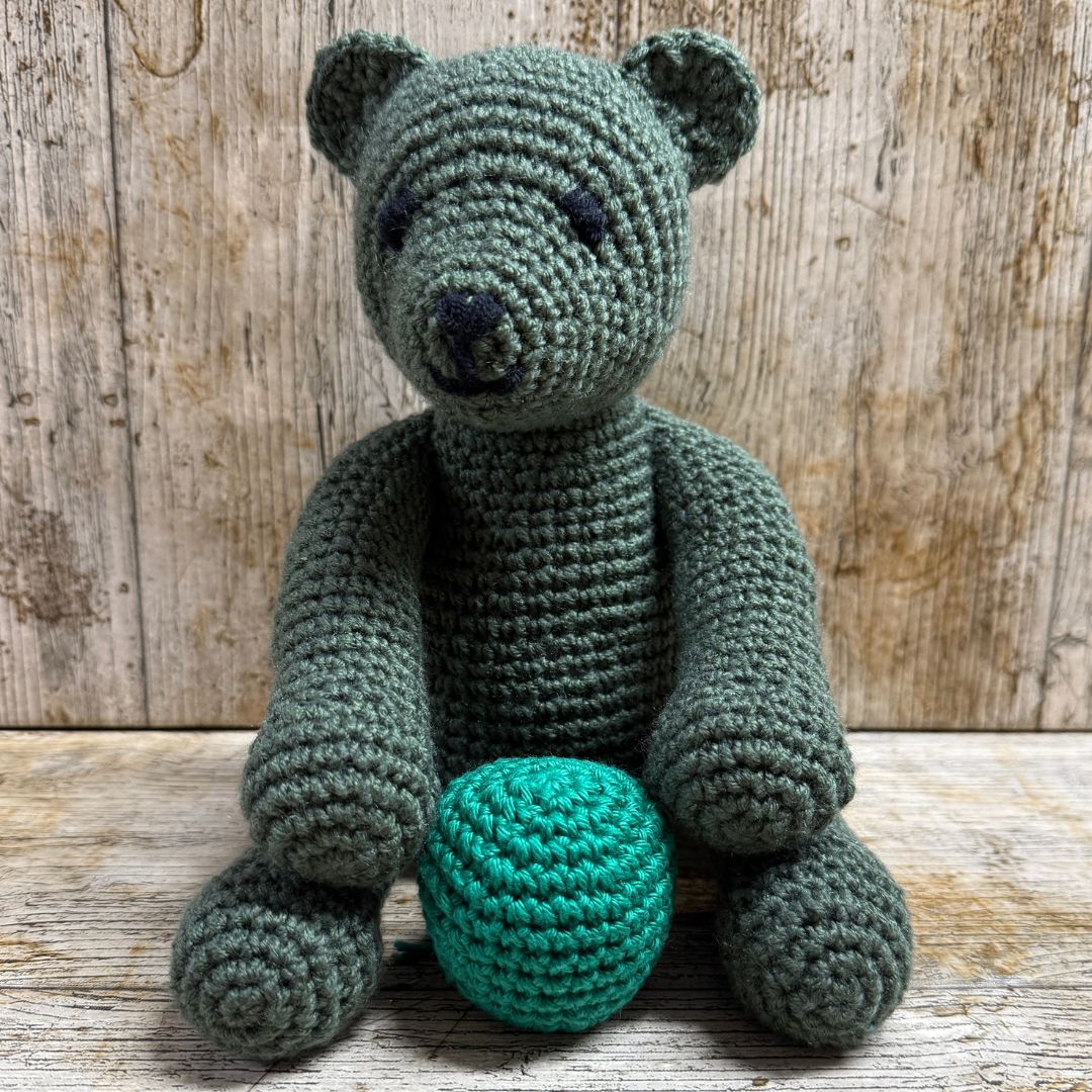 Crocheted bear with a teal ball on a wooden surface