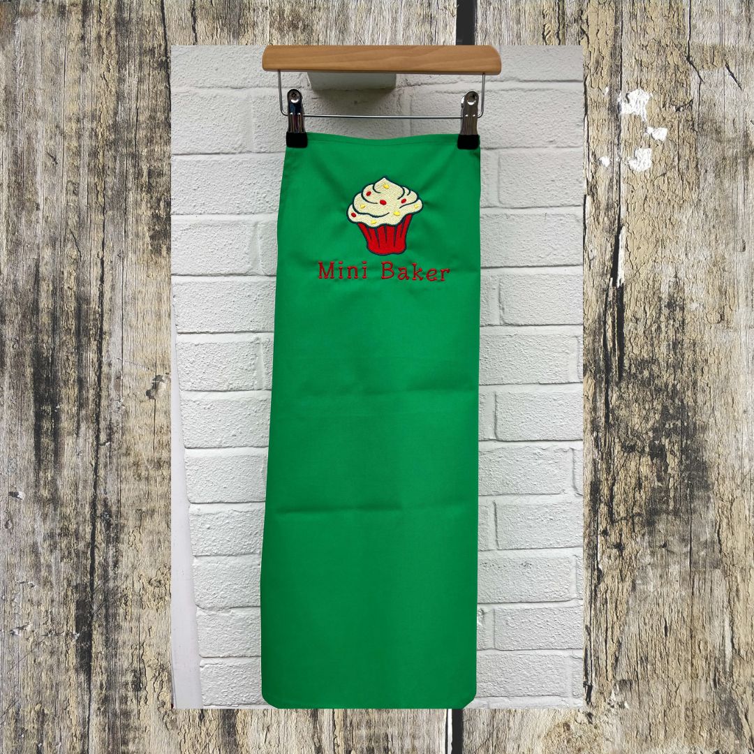 This photo shows the full length of the apron with Mini Baker words and a beautifully embroidered cupcake, made to order at Coralie's Crafts & gifts