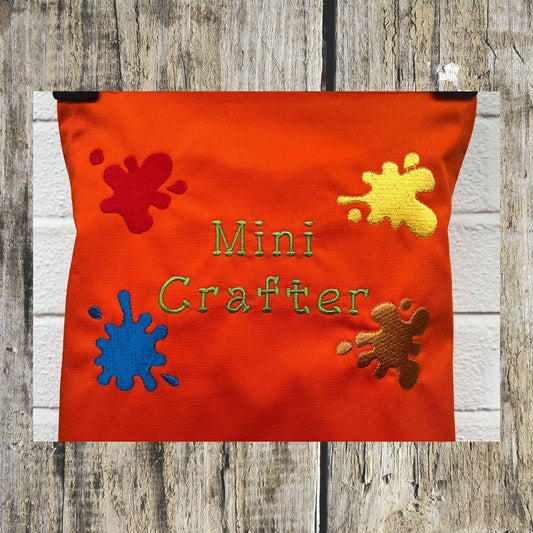 This wonderful orange Mini Crafter Apron has embroidered splodges of paint on it and the wording  Mini Crafter, all embroidered by Coralie at Coralie's Crafts & Gifts.