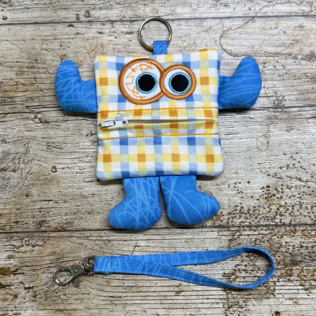 Money Monster purse keychain with checked body and blue limbs on a wooden surface