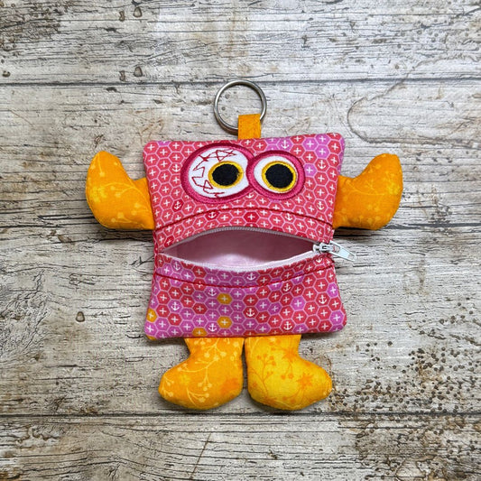 Pink and yellow money monster purse pouch with a zipper on a wooden surface