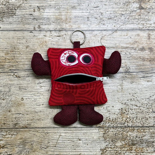 Red Money monster called Swirlie Stash with a keychain and a zipper for a mouth on a wooden surface