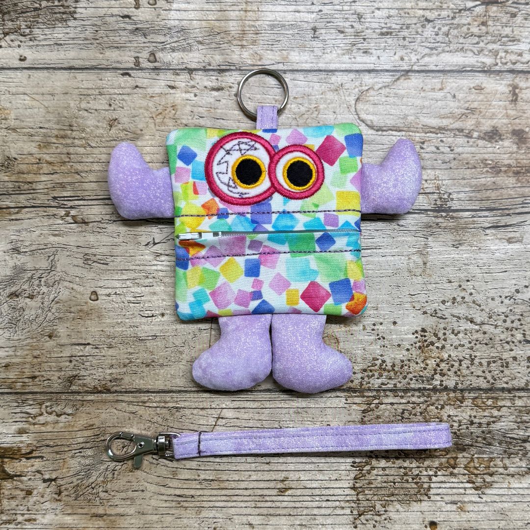 Colourful monster-shaped children's purse  with lilac arms and legs with a zipper on a wooden surface, with a wrist strap
