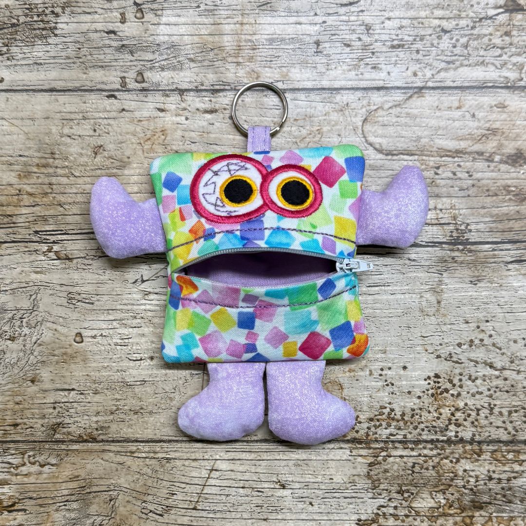 Colourful monster-shaped children's purse  with lilac arms and legs with a zipper on a wooden surface