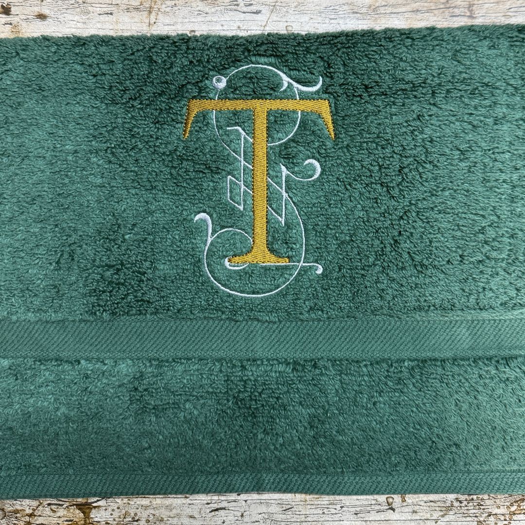 Green towel with embroidered letter 'T' on a wooden surface