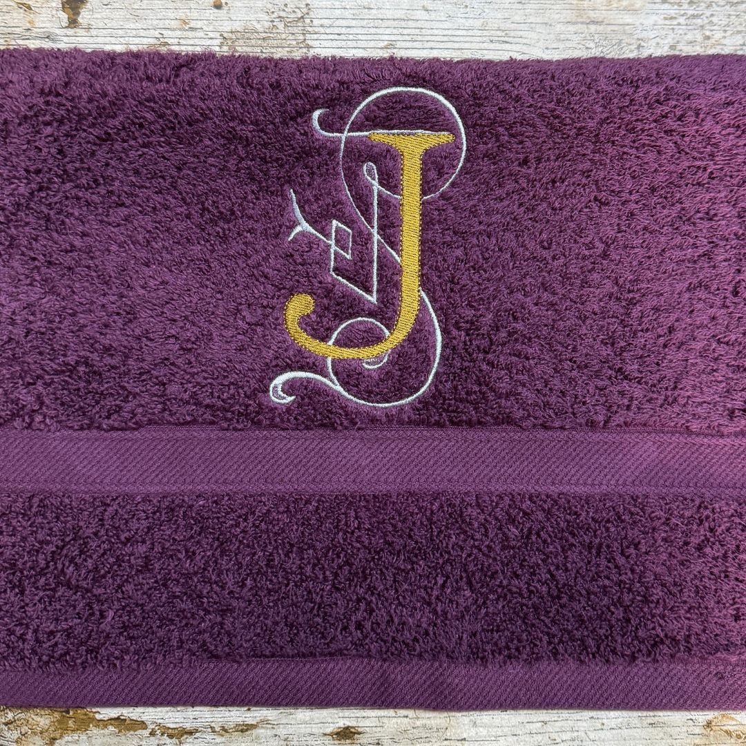 Purple towel with a gold and white embroidered letter 'J' on a wooden surface